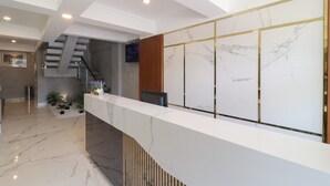 A modern reception area with a marble counter, a staircase, and a television mounted on the wall. - Flamenco Urban Living (Jakarta)