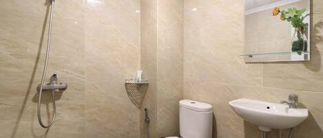 A bathroom with a shower, toilet, sink, and a mirror with a vase of flowers.