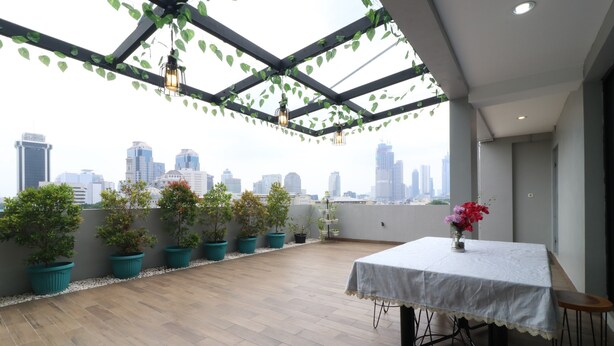 A rooftop terrace with a table and chairs, potted plants, and a city skyline view. - Flamenco Urban Living (Jakarta)