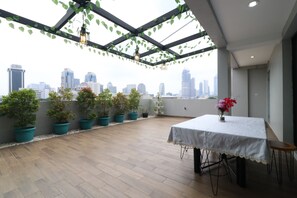 A rooftop terrace with a table and chairs, potted plants, and a city skyline view. - Flamenco Urban Living (Jakarta)