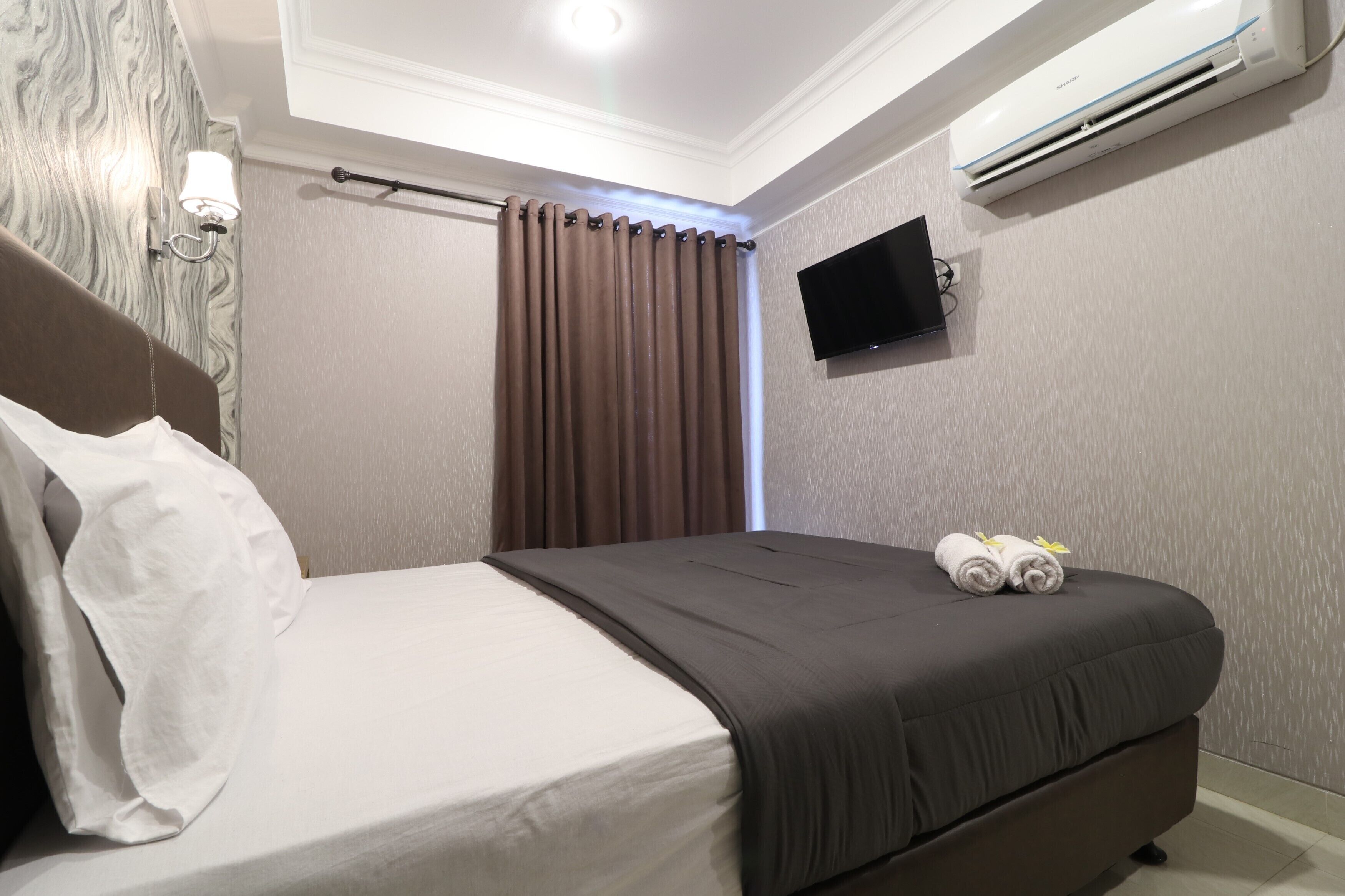 Una habitación de hotel con cama, televisor de pantalla plana en la pared y aire acondicionado.