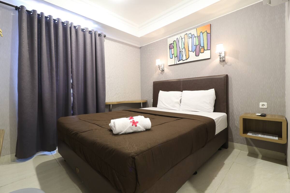 A hotel room with a large bed, a bedside table, a wall-mounted artwork, and a curtain.