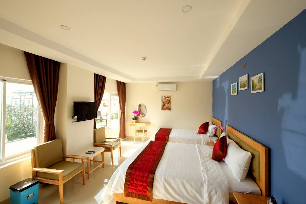 Habitación de hotel con dos camas, un escritorio, una silla, un televisor y una ventana con cortinas.
