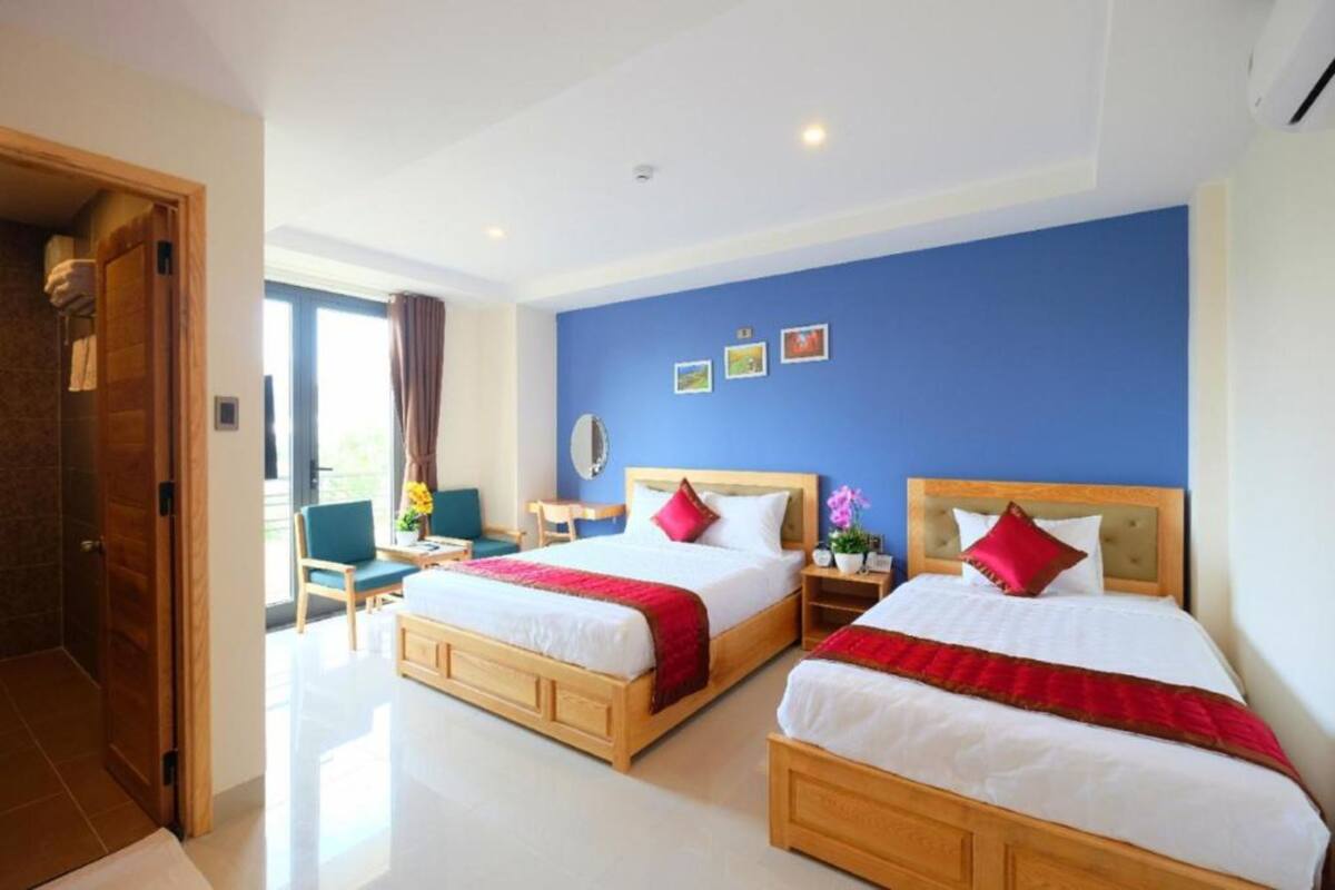 Una habitación de hotel con dos camas, una puerta de madera, una pared azul y una ventana con cortinas.