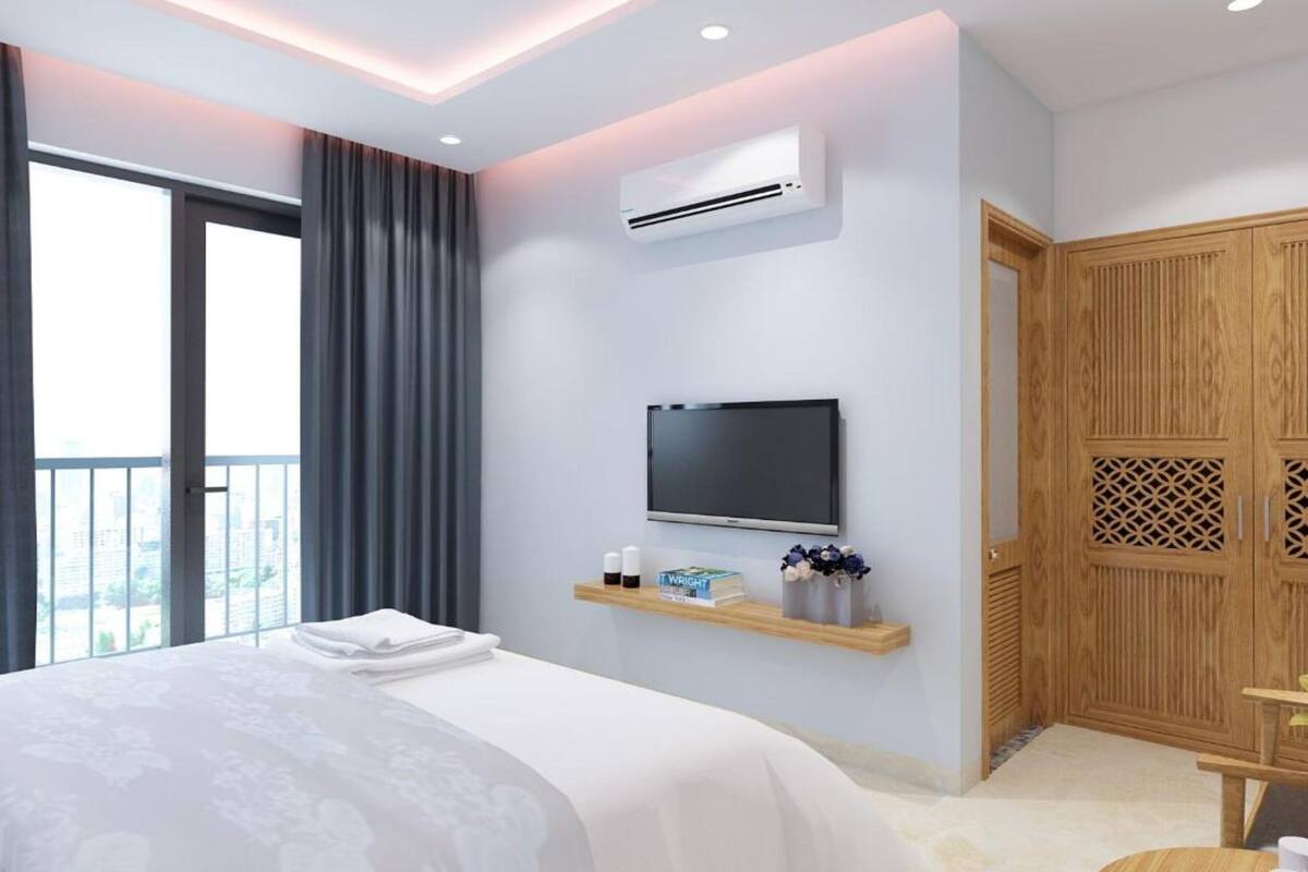 Una habitación de hotel moderna con una cama grande, un televisor de pantalla plana, un equipo de aire acondicionado, un armario de madera y un balcón con vistas a la ciudad.