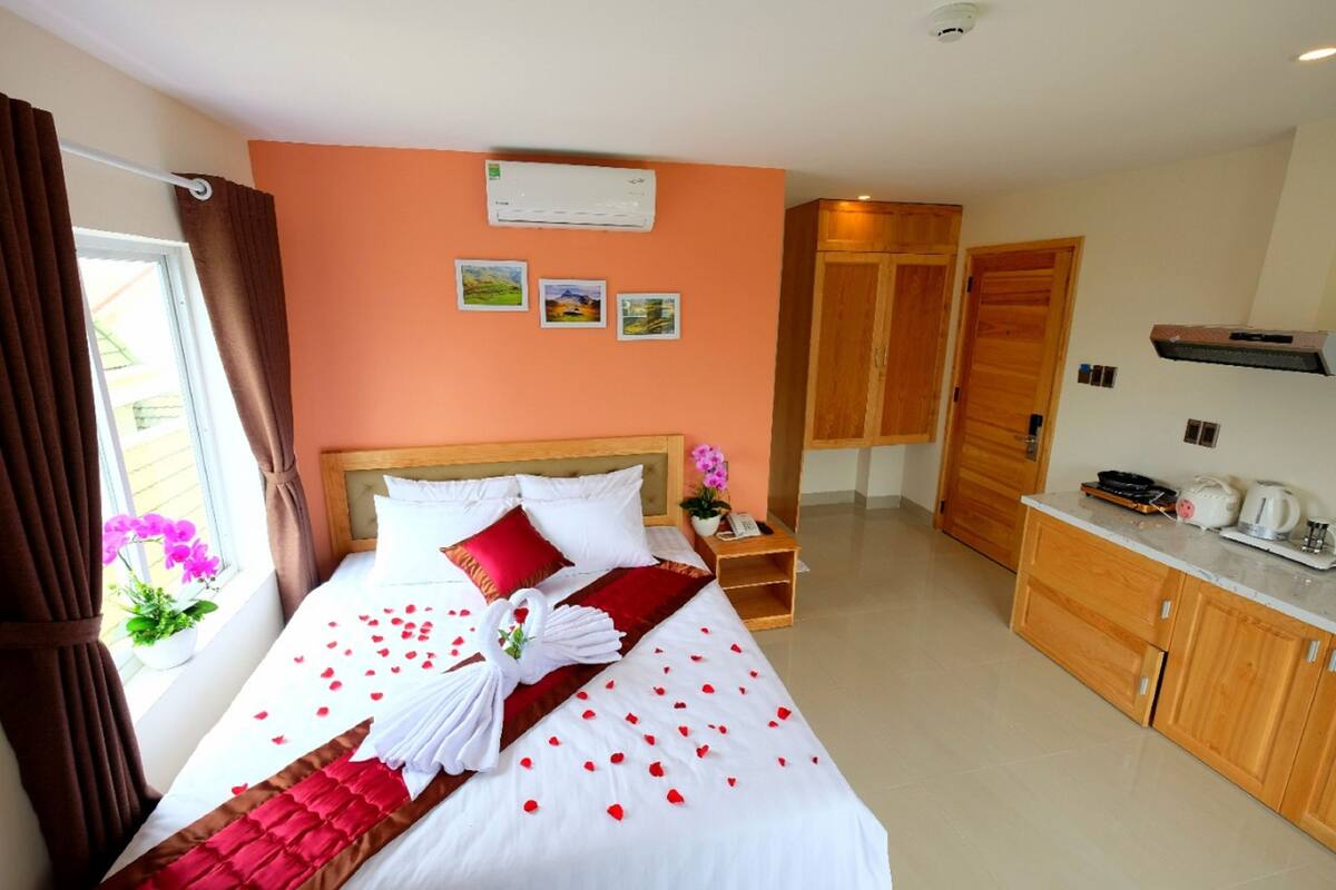 Una habitación de hotel con una cama, un armario de madera, una mesita y una ventana con cortinas.