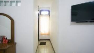 A narrow hallway with a tiled floor, a door at the end, and a flat-screen TV mounted on the wall.