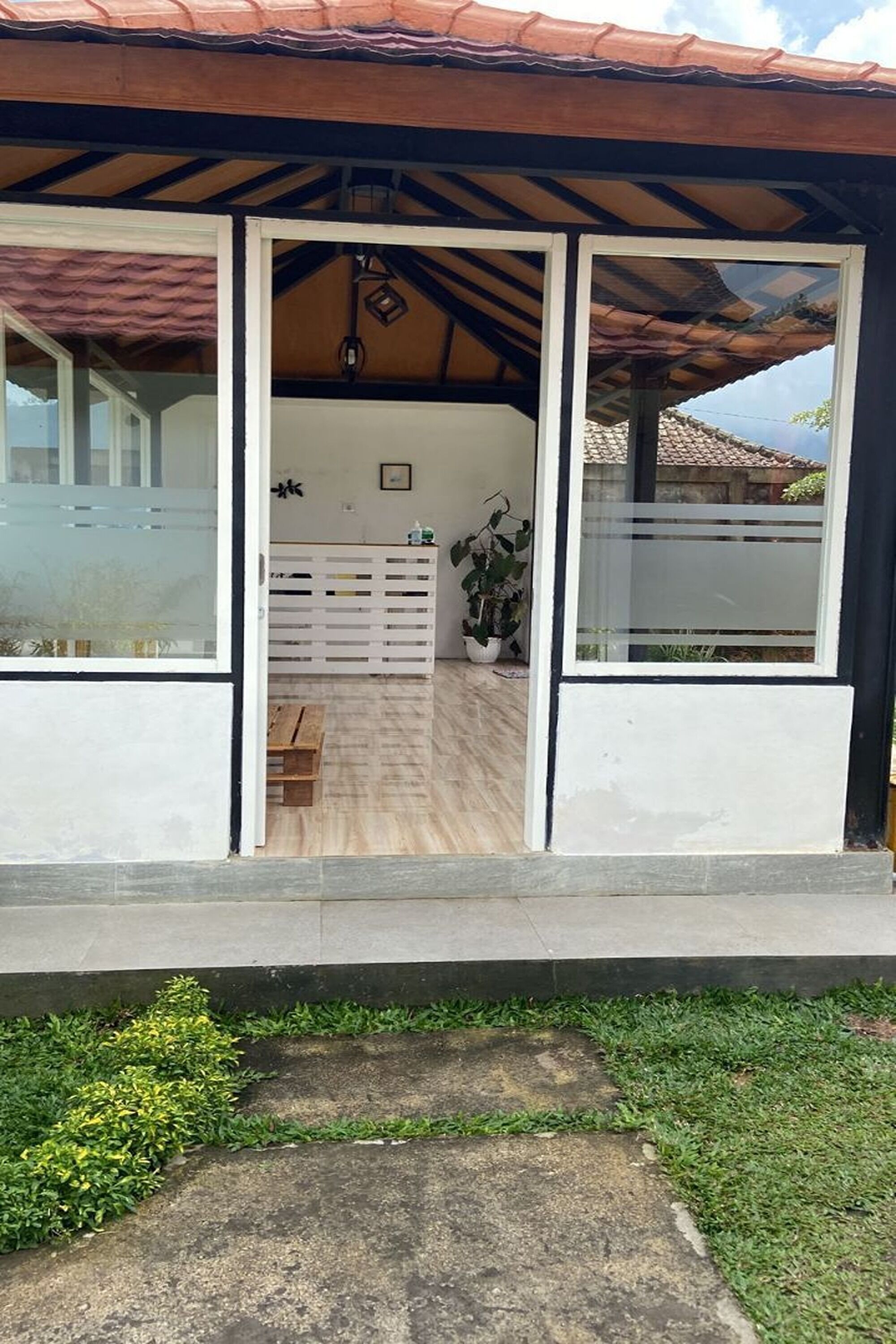 A covered outdoor area with a wooden bench, a white fence, and a potted plant.