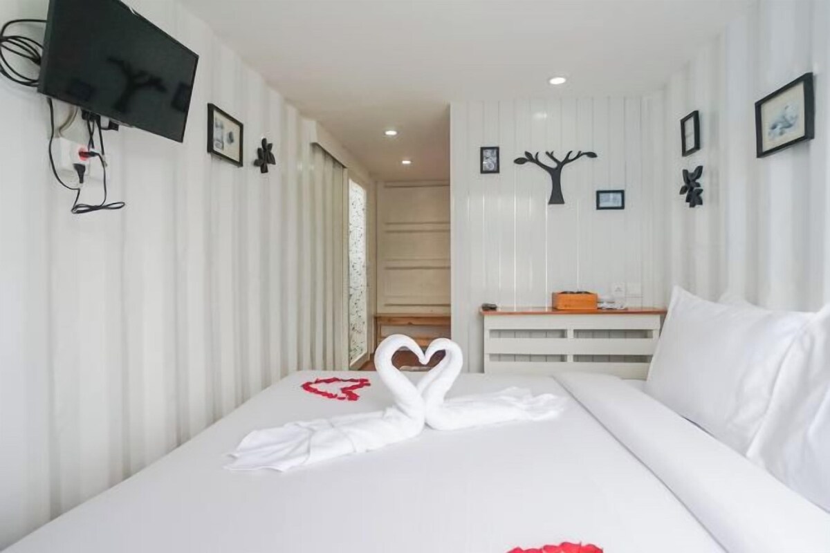 A hotel room with a bed, a TV mounted on the wall, and a wall-mounted shelf with a picture frame.