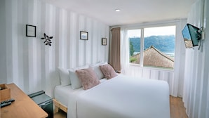 A hotel room with a bed, a wooden desk, and a window with a view of a building and trees.