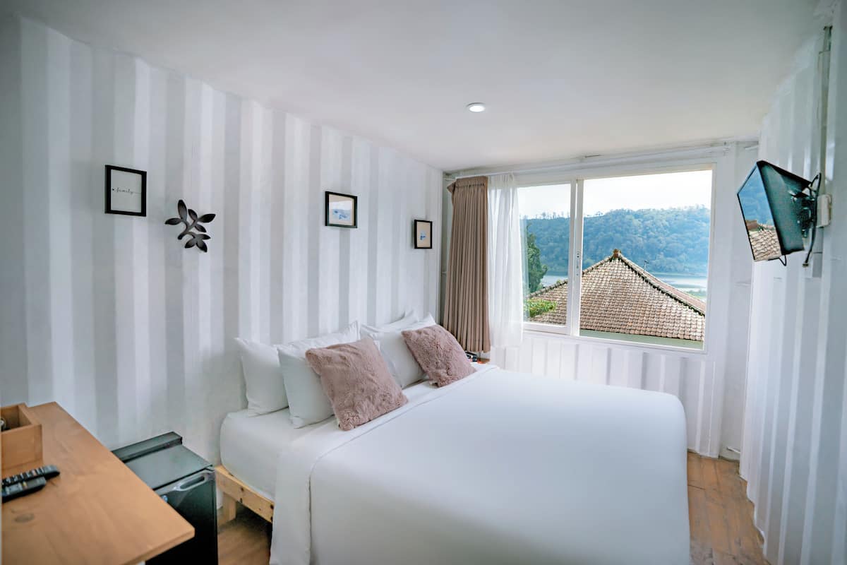 Habitación de hotel con cama, un escritorio de madera y ventana con vistas a un edificio y árboles.