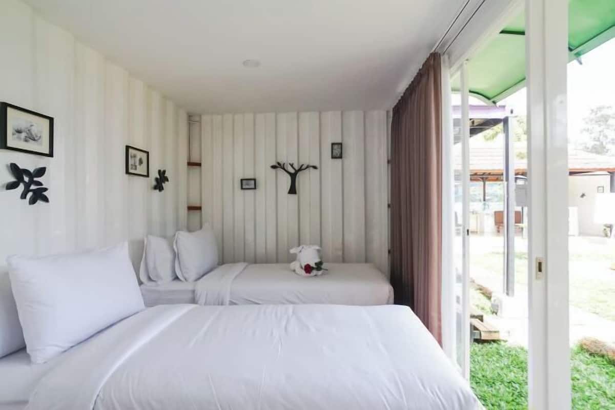 Una habitación con dos camas, un toldo verde, decoración de pared con motivos de árbol y cuadros enmarcados.
