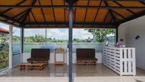A covered outdoor seating area with two sofas, a small table, and a white storage unit.