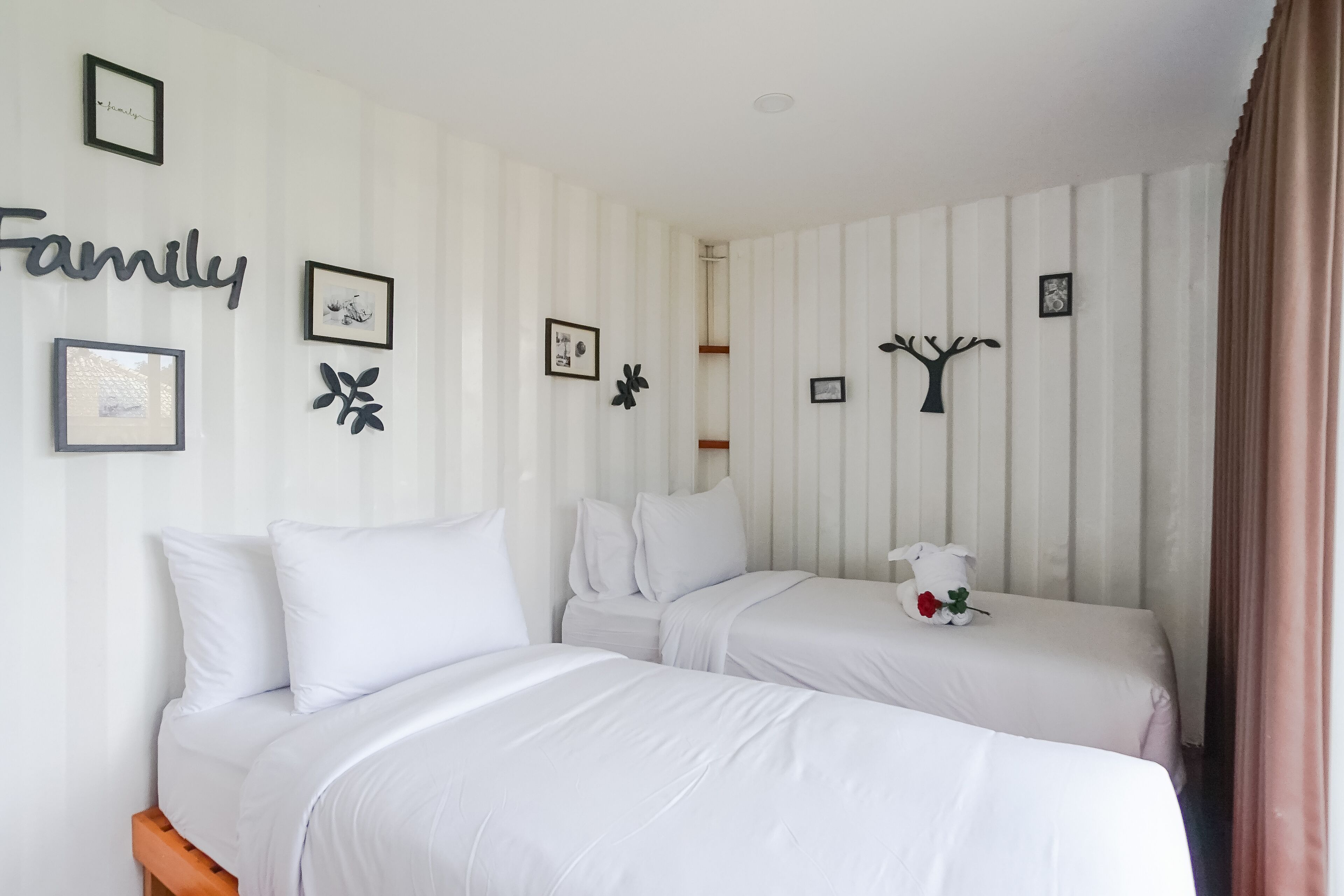 Habitación de hotel con dos camas, ropa blanca y una pared decorada con cuadros y un cartel que dice 'Familia'.
