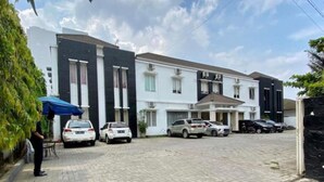 A residential building with a modern design, featuring a driveway with parked cars and a person standing by a blue umbrella. - Roemah Moesi Medan (Medan)