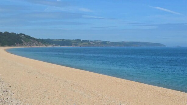 Une plage de sable fin, avec des eaux calmes et une côte visible au loin.