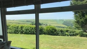 Une pièce dotée de grandes fenêtres donnant sur un paysage verdoyant, avec des champs et des arbres.