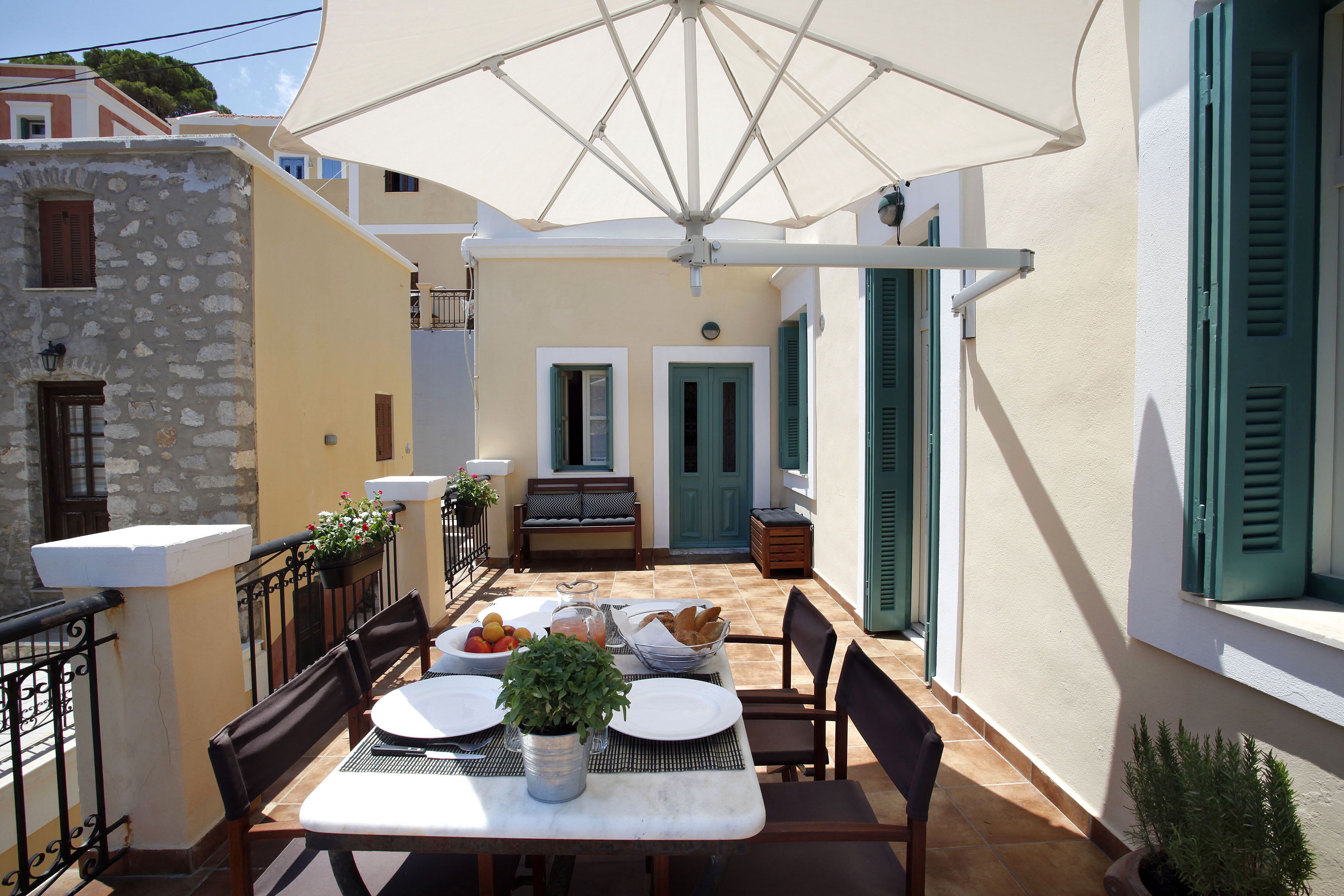 Un espace de restauration en plein air avec une table dressée pour deux personnes, entourée de chaises, d’un grand parasol et d’une plante en pot.