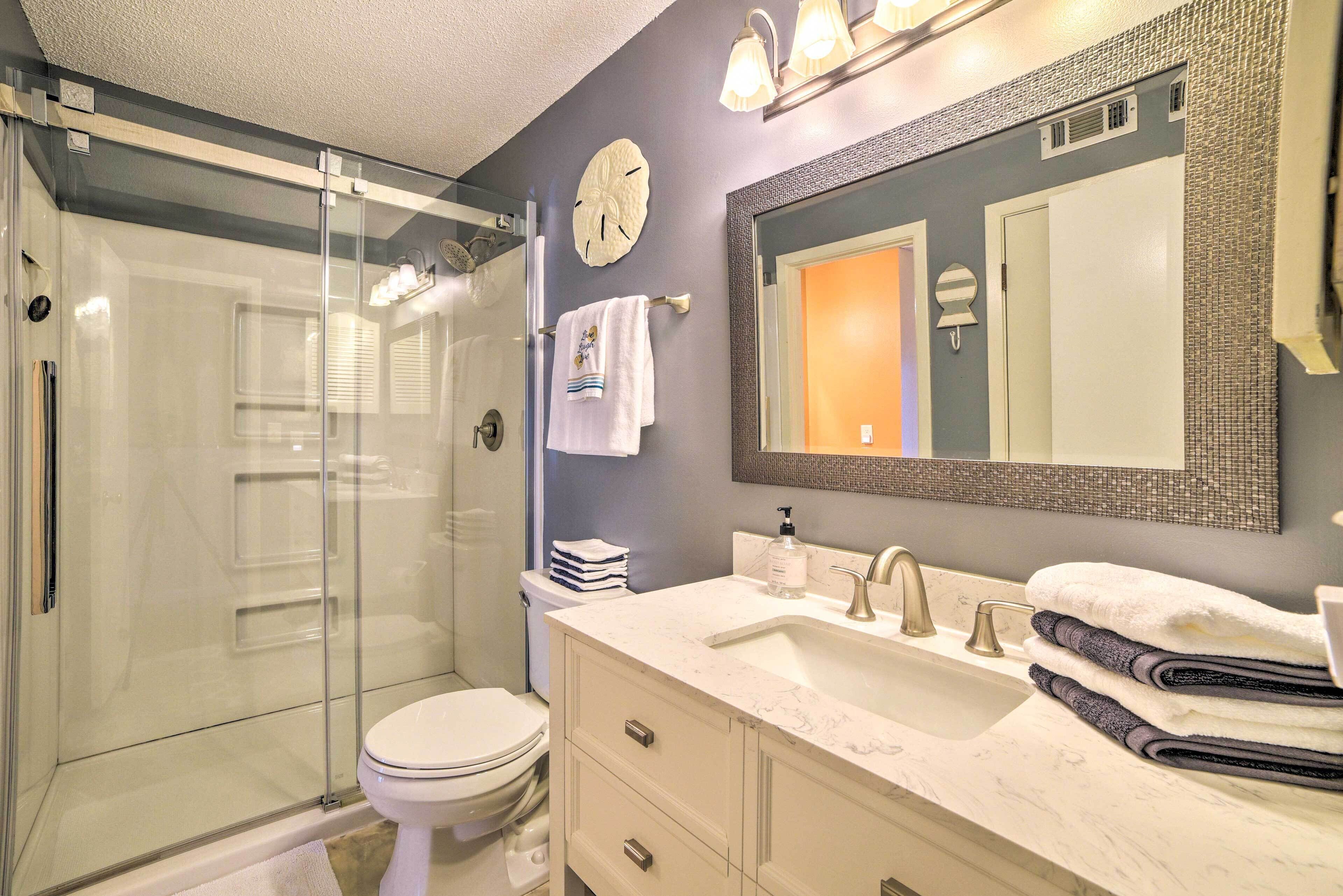 A bathroom with a glass shower enclosure, a white toilet, a vanity with a sink, and a large mirror.