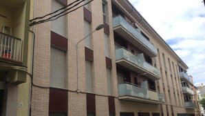 Un edificio residencial de varios pisos con balcones, una furgoneta estacionada y una señal de tráfico que indica zona de no estacionamiento.