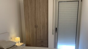 Un dormitorio con dos camas, un armario, una mesita de noche con lámpara y una puerta corredera a un balcón.