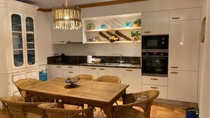 Una cocina moderna con armarios blancos, horno empotrado y comedor con mesa de madera y sillas de mimbre.