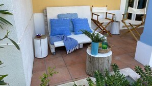 Cómodo espacio al aire libre con un sofá blanco, cojines azules y una mesita baja con bebidas y plantas.