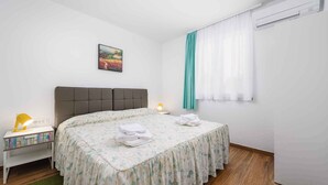 A bedroom with a bed, bedside table with a lamp, a picture on the wall, and an air conditioning unit. - Holiday apartment with internet and air conditioning near the sea (Umag)