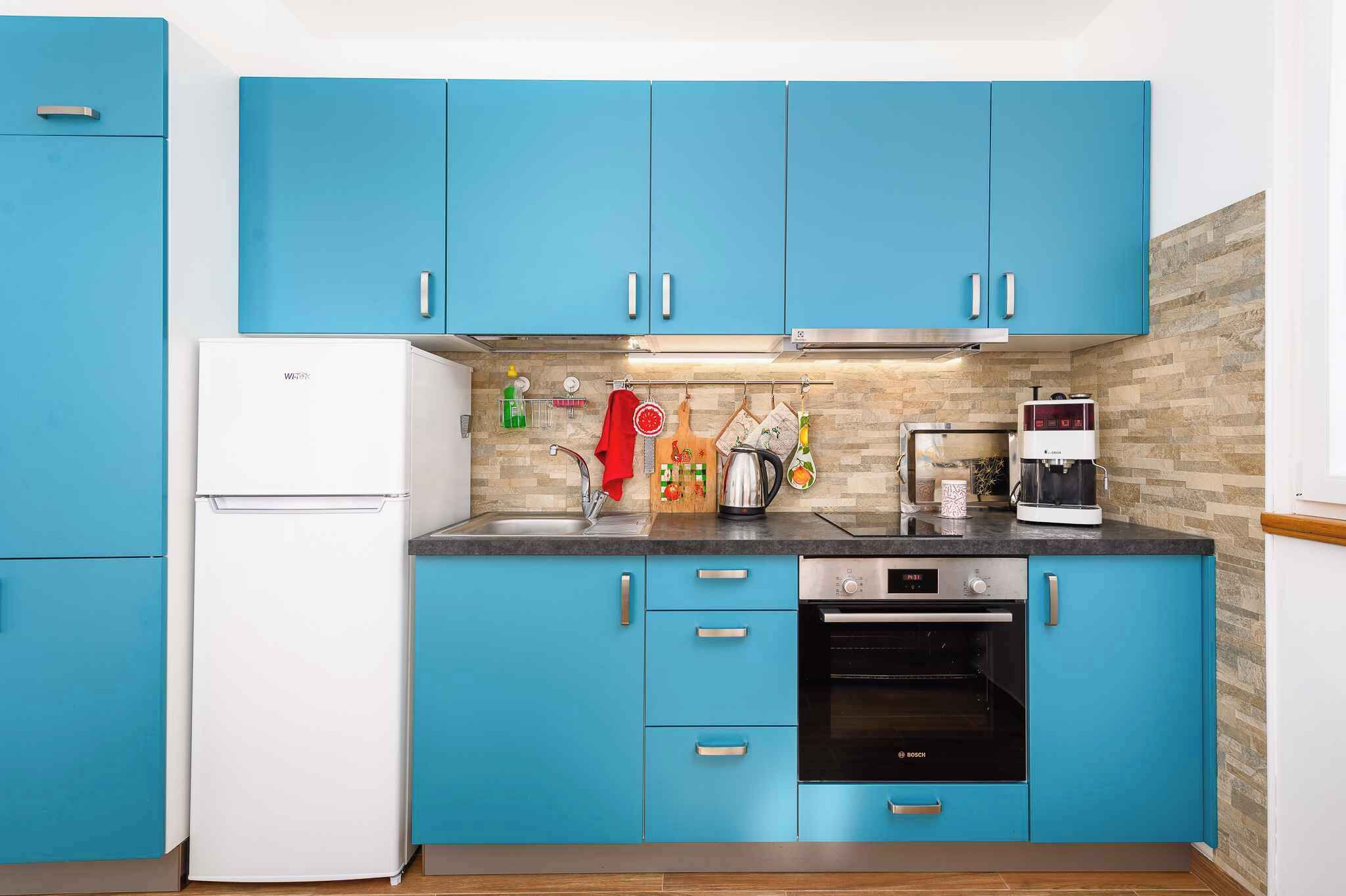 Una cocina con armarios azules, un refrigerador blanco, un horno Bosch y una cafetera.