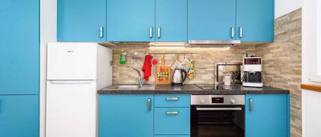 Una cocina con armarios azules, un refrigerador blanco, un horno Bosch y una cafetera.