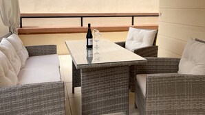Ein überdachter Außenbereich mit Korbmöbeln und einem Tisch, mit einer Flasche und einem Glas.