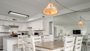 A modern kitchen with white cabinetry, a wooden dining table, and pendant lighting. - Two Bedroom Condo With Great Side View of the Ocean (Ocean City)