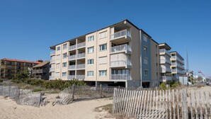 A multi-story building with balconies, situated on a sandy beach with a wooden fence in the foreground. - Two Bedroom Condo With Great Side View of the Ocean (Ocean City)