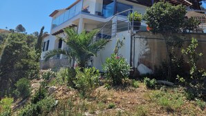 Una casa de dos pisos con balcón, rodeada de follaje y árboles.