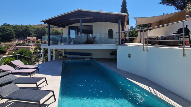 Un área de piscina moderna con sillones reclinables, un porche techado y vistas al paisaje circundante.