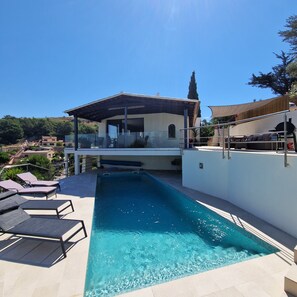 A modern pool area with lounge chairs, a covered patio, and a view of the surrounding landscape.