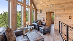 Una cabaña espaciosa con ventanas amplias, una zona de estar acogedora con mobiliario de cuero y un interior de madera.