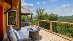 Una terraza de madera con un hogar de piedra, asientos exteriores y vistas al bosque.