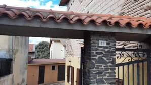 Uma passagem estreita com uma parede de pedra e um telhado de telhas. É visível um portão com o número 48.