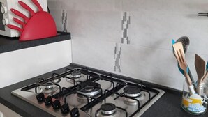 Uma cozinha com fogão a gás, suporte vermelho para espátulas e um pote de utensílios.