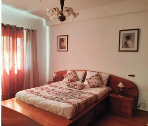 A bedroom with a wooden bed, floral bedding, a nightstand with a lamp, and two framed pictures on the wall. - Villa quinta São Jorge (Setúbal)