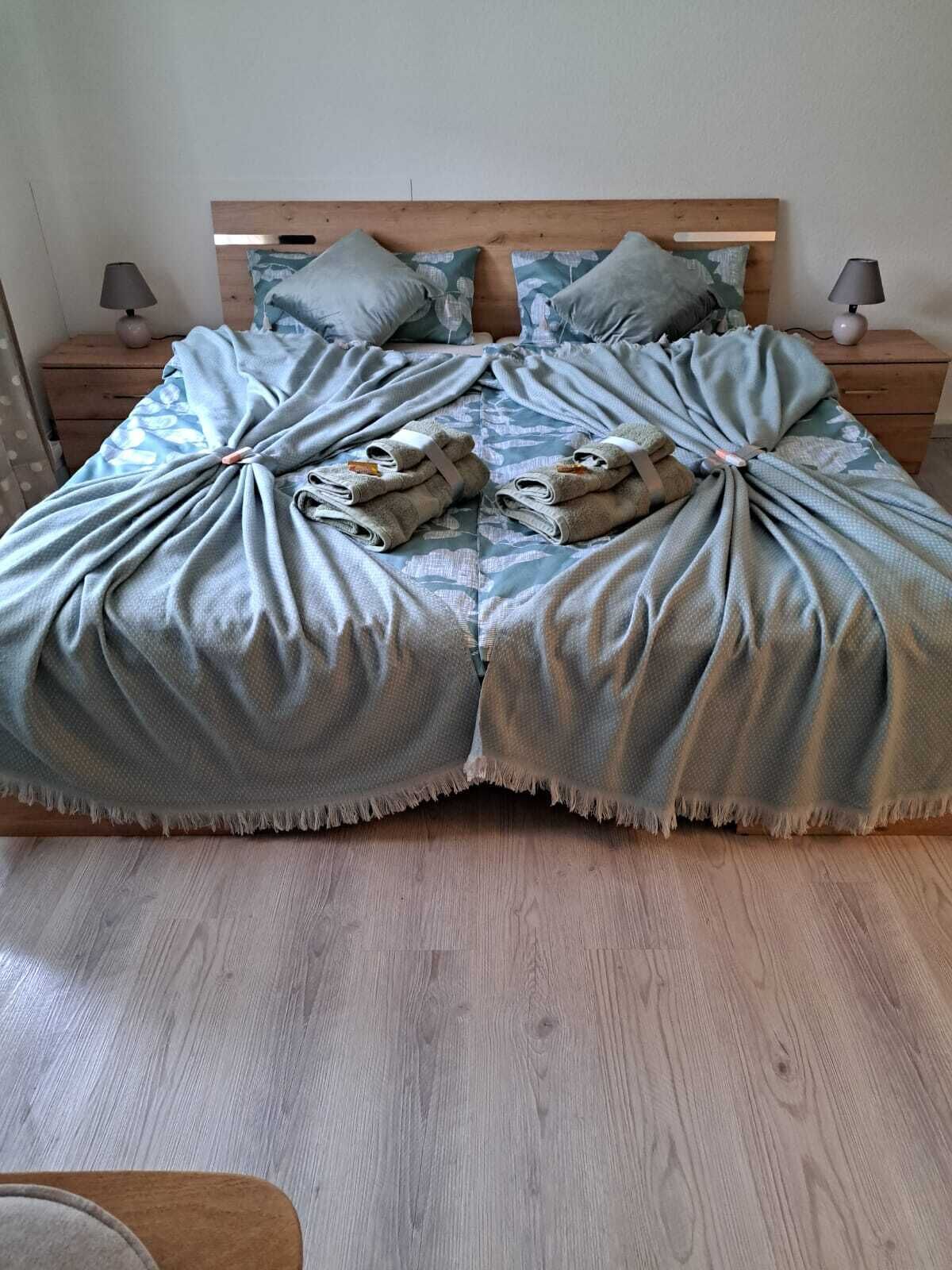 Una cama con cabecera de madera, ropa de cama gris y dos lámparas de noche.