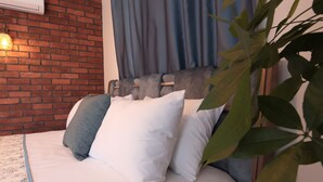 A bed with white and grey pillows, a floral bedspread, and a brick wall with a hanging light fixture. - Trend Cunda Otel (Ayvalik)