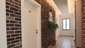 A hallway with a brick wall, a white door labeled '10', a potted plant, and patterned floor tiles. - Trend Cunda Otel (Ayvalik)