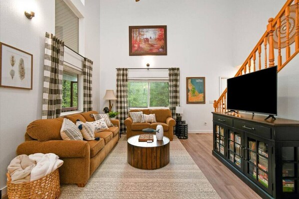 A living room with two sofas, a coffee table, a TV, and a staircase. - Cascade Cabin, Walk to the Lake, Amazing Deck! (Cascade)