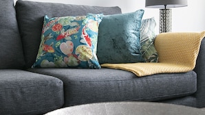 En grå sofa med farverige puder og et vævet tæppe. Et rundt bord med citroner står foran sofaen.