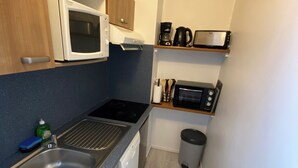 Ett kompakt kök med en mikrovågsugn, brödrost och kaffebryggare på en hylla, en diskho med en flaska diskmedel och en papperskorg.