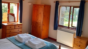 Un dormitori amb llit, armari de fusta, tocador i finestra amb cortines.