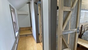 Een smalle gang met houten vloeren, een plafondlamp en een grote houten deur.
