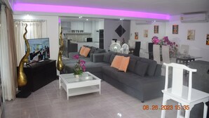 Un salon moderne avec un canapé gris, une table basse blanche et un fauteuil blanc. On y trouve un téléviseur posé sur un meuble noir, ainsi que des objets décoratifs sur une commode noire.